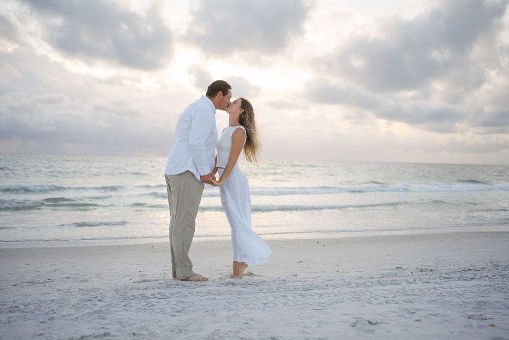 Couple kissing on an empty stretch of white sand beach at sunset