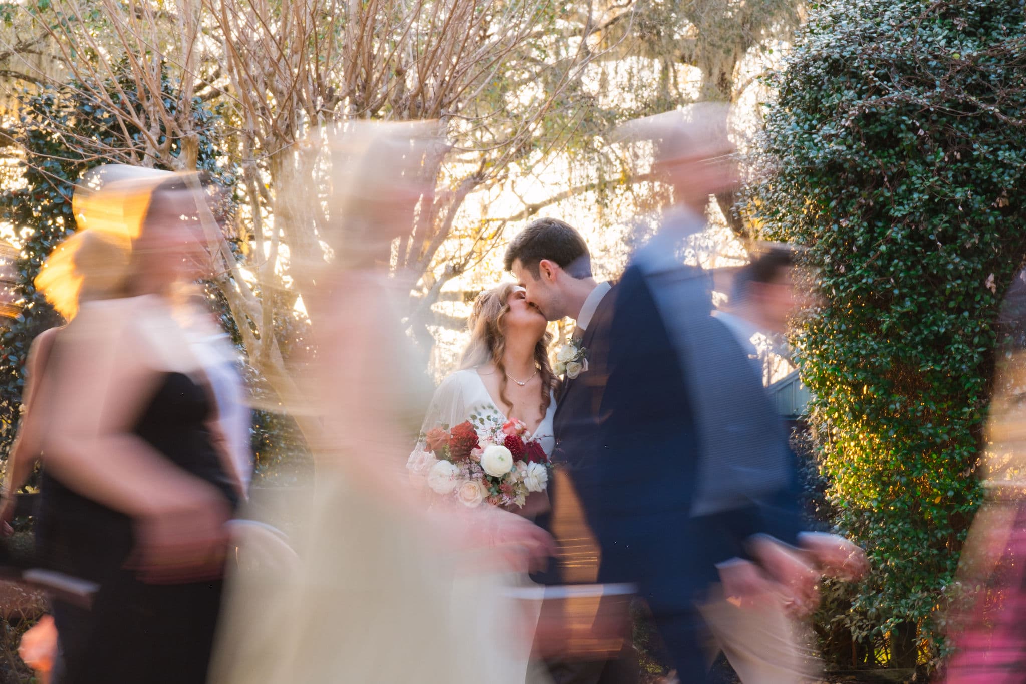 Couple kissing while guests move around them in motion blur, golden garden light