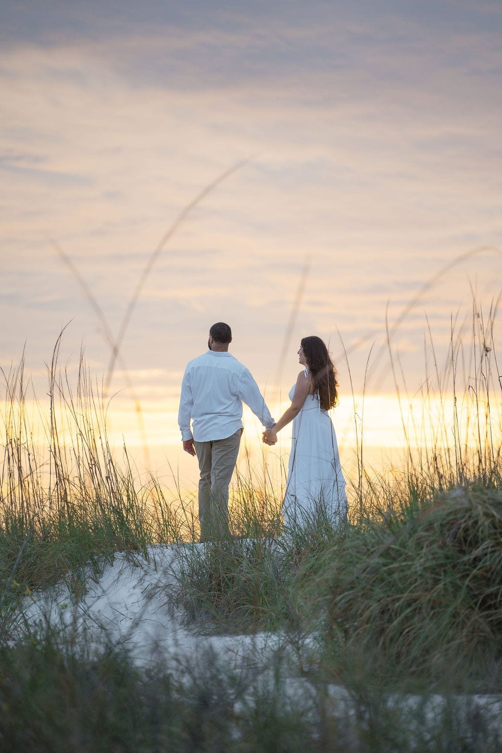Couple holding hands walking through dunes golden sunset