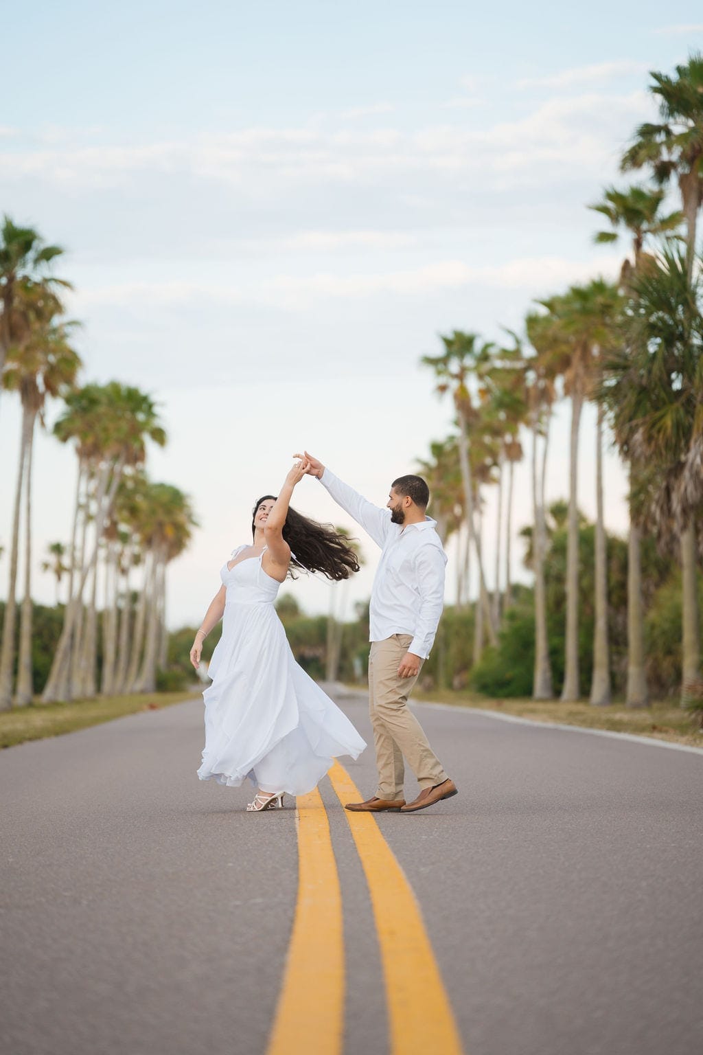 Couple twirling on palm lined road Tampa engagement