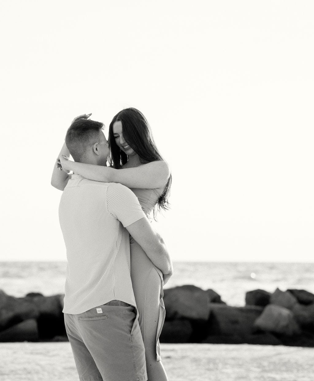 Black and white couple lifted embrace beach jetty rocks