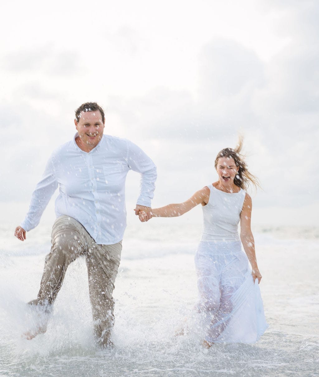 Couple running splashing through waves laughing gulf beach