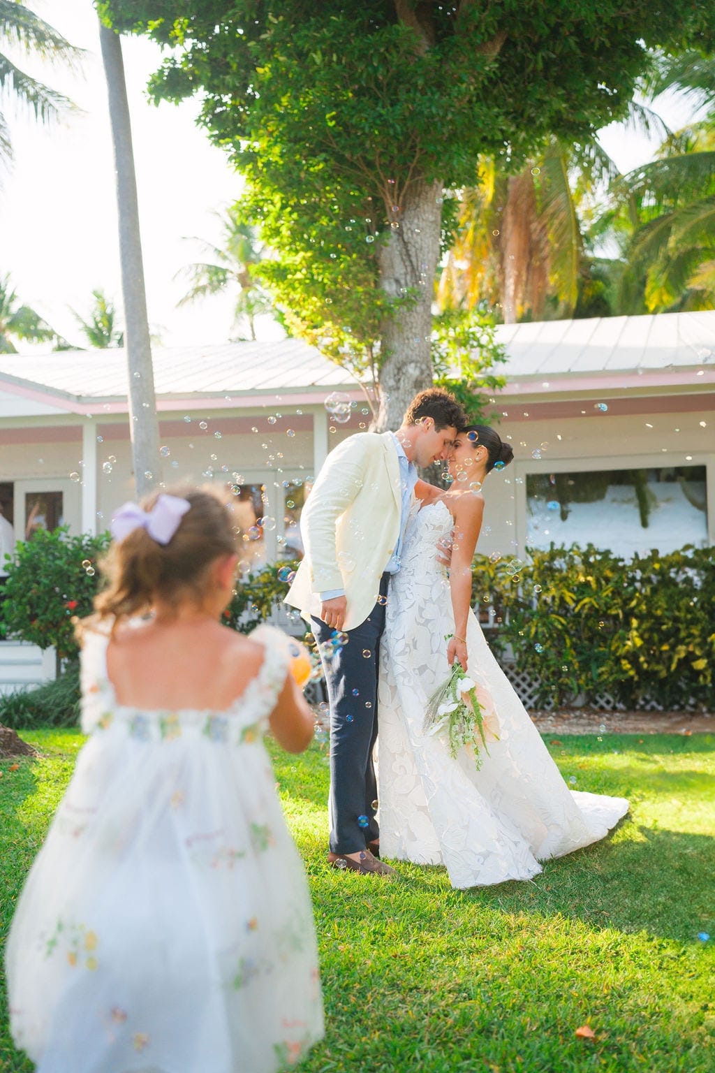 Bride and groom forehead touch flower girl blowing bubbles