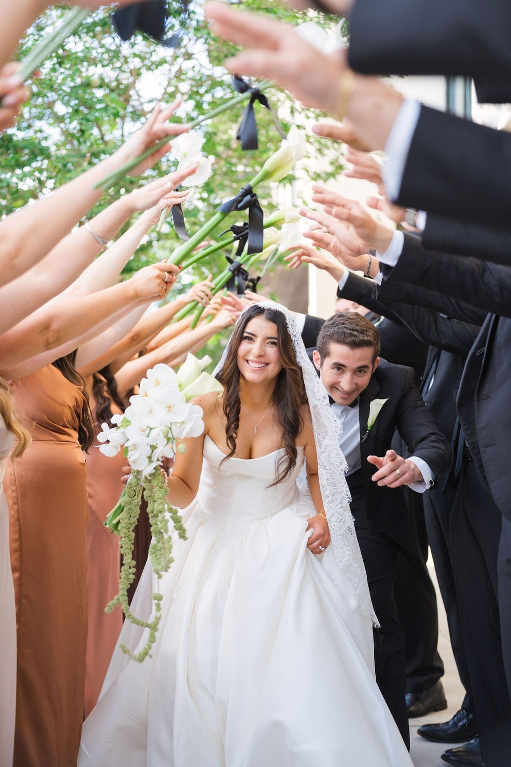 Bride and groom walk through wedding party flower tunnel