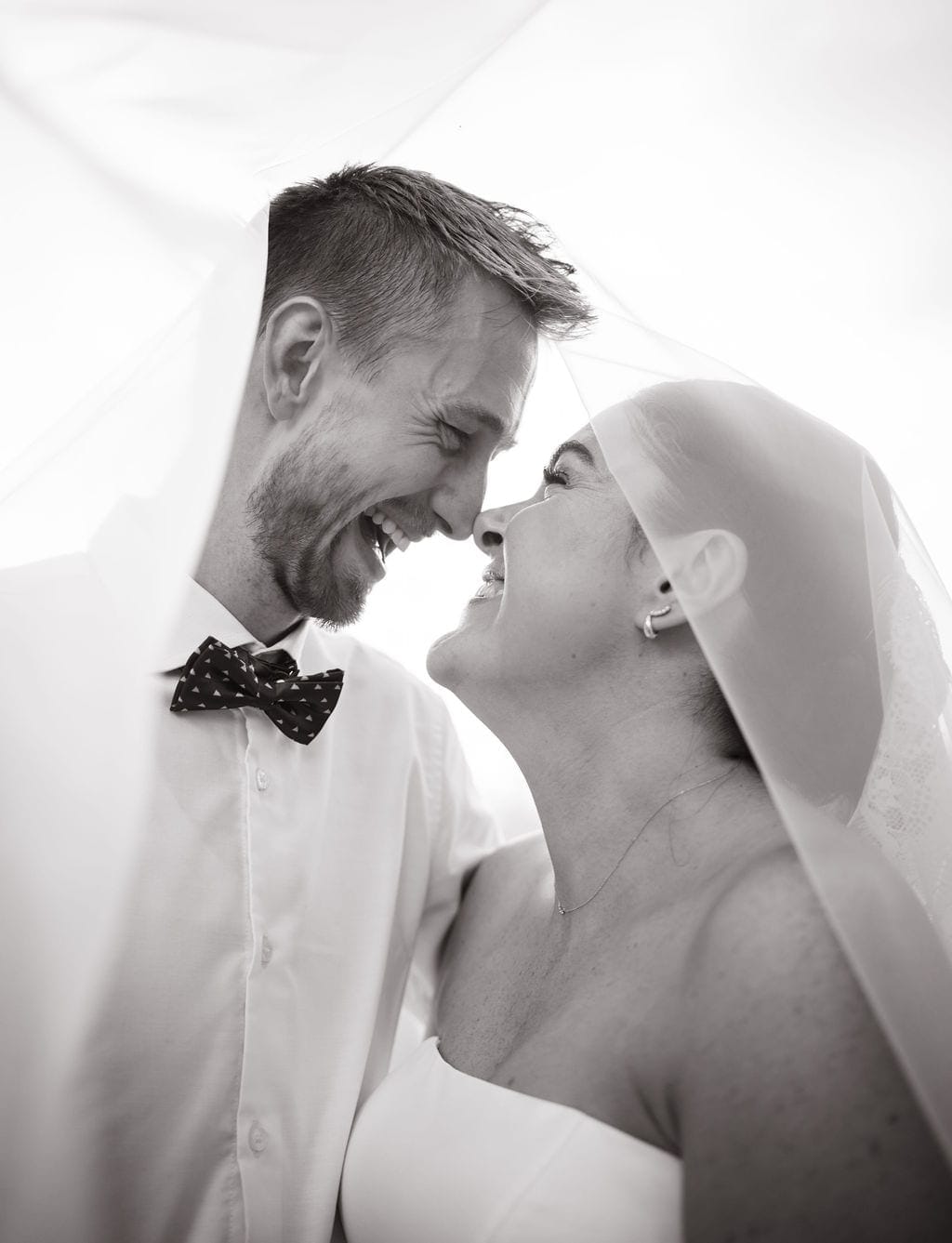 Black and white bride and groom laughing under veil