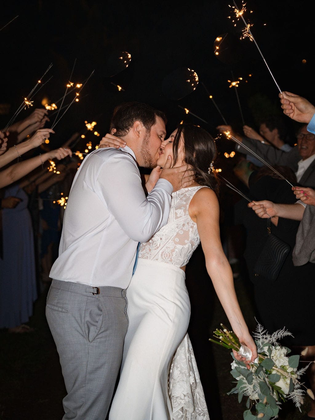 Bride and groom kissing during sparkler exit at night