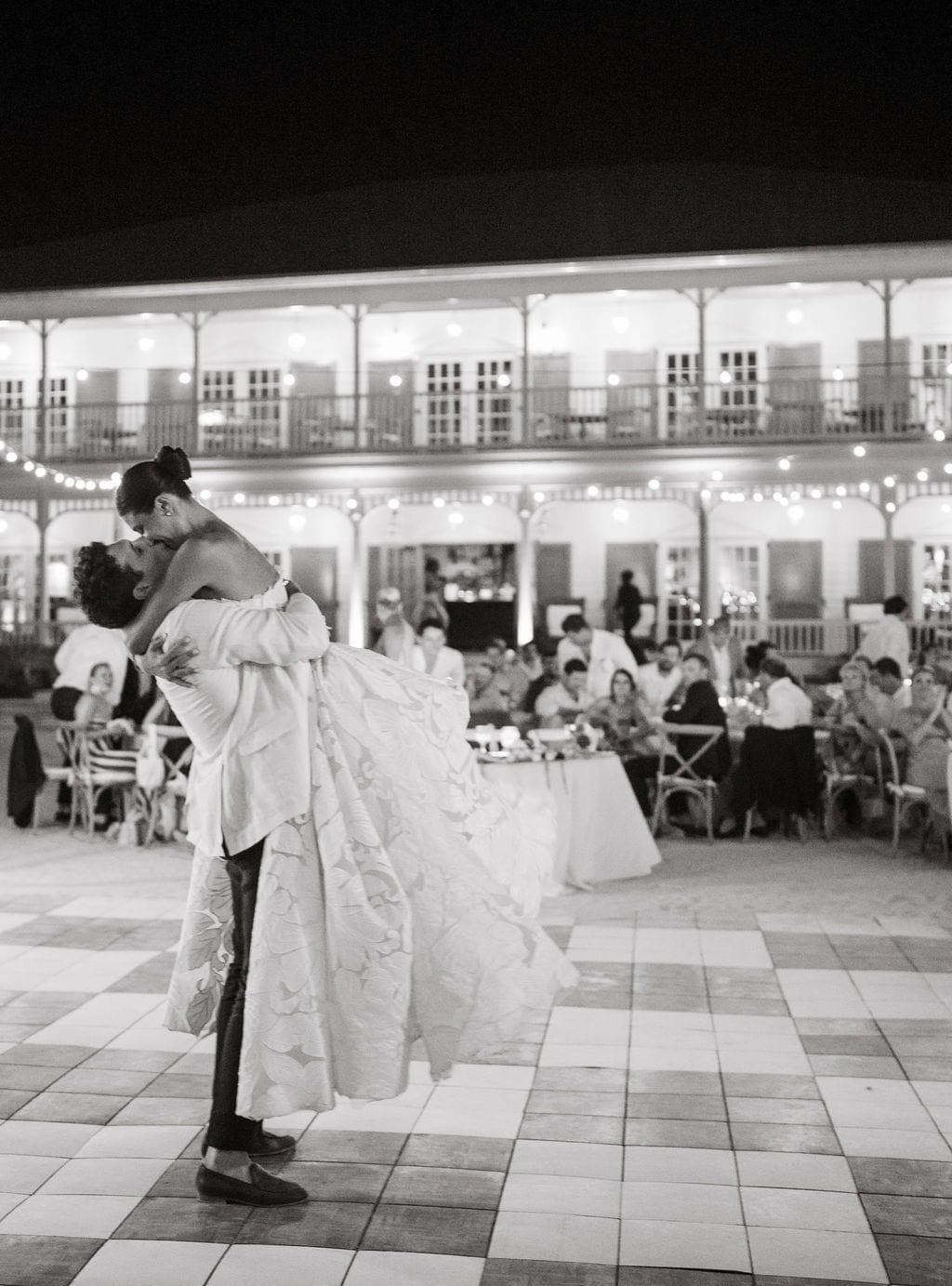 Groom lifting bride first dance kiss string lights reception
