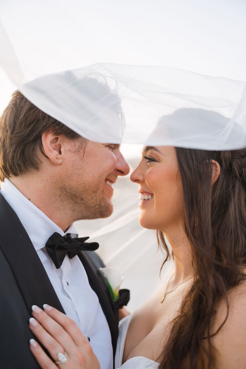 Bride and groom laughing under veil golden hour portrait