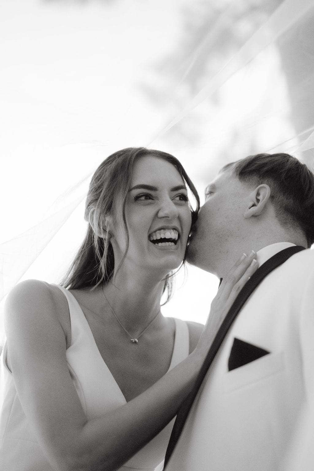 Groom kissing laughing brides cheek under veil