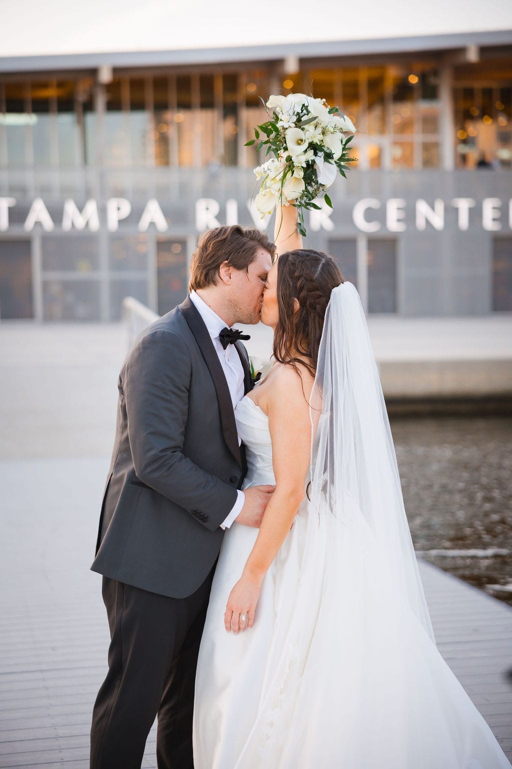 Bride and groom kiss bouquet raised waterfront Tampa