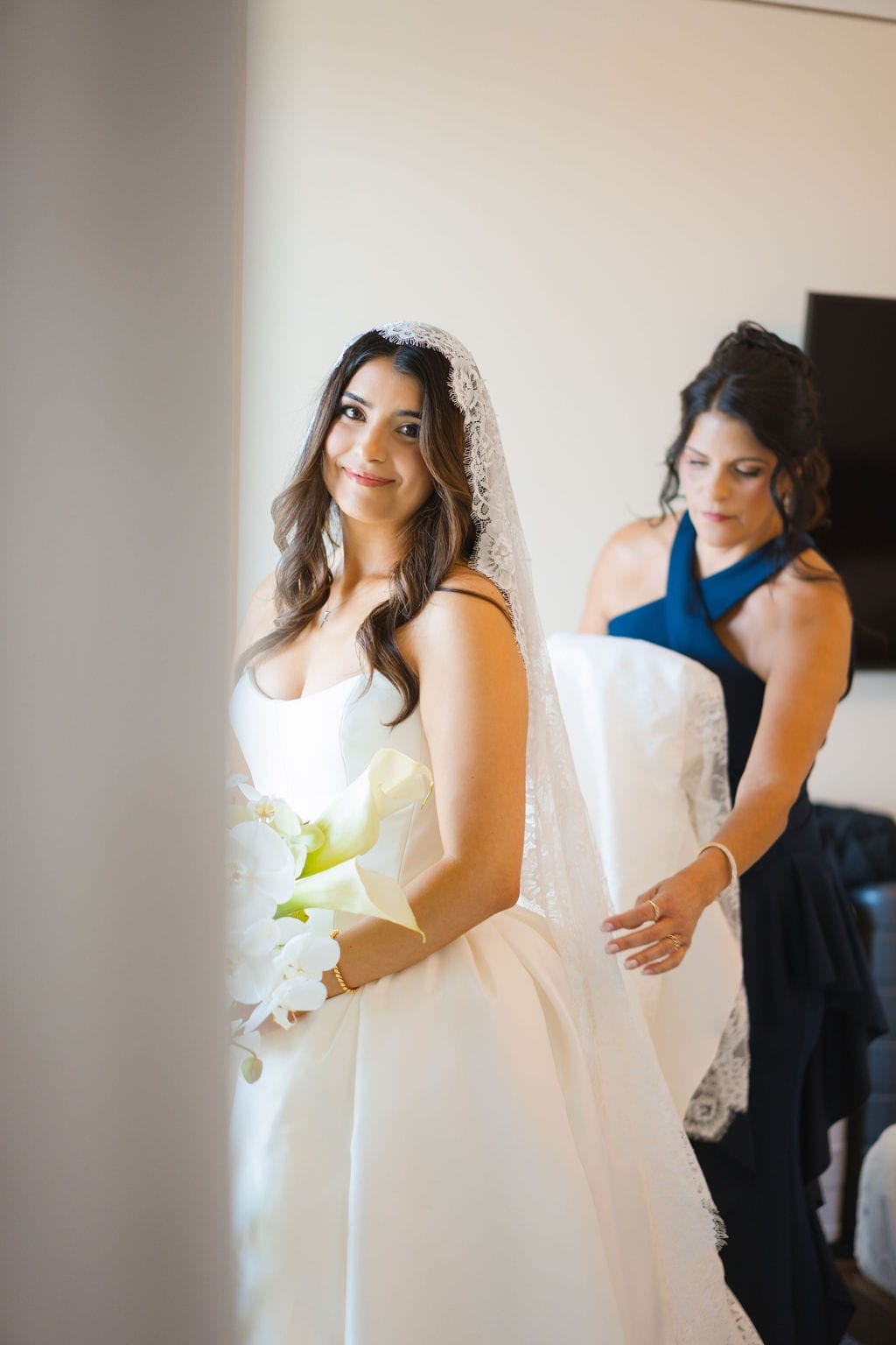 Bride in lace mantilla veil mother adjusting gown