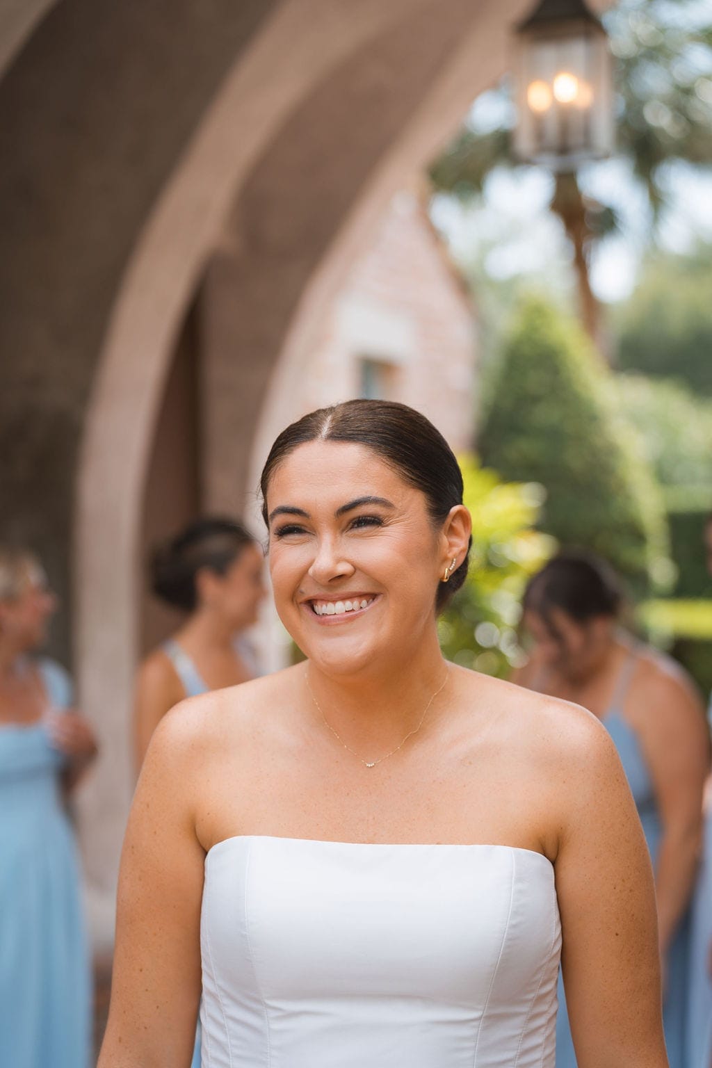 Bride smiling under stone arches white strapless gown