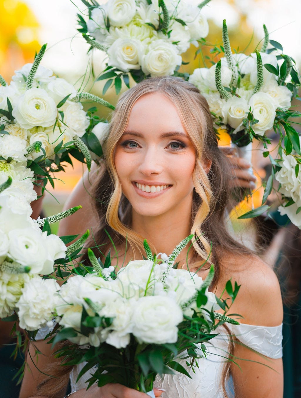 Bride framed by white rose bouquets held by bridesmaids