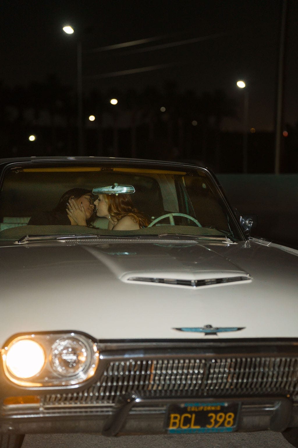 Newlyweds kissing in vintage convertible getaway car night