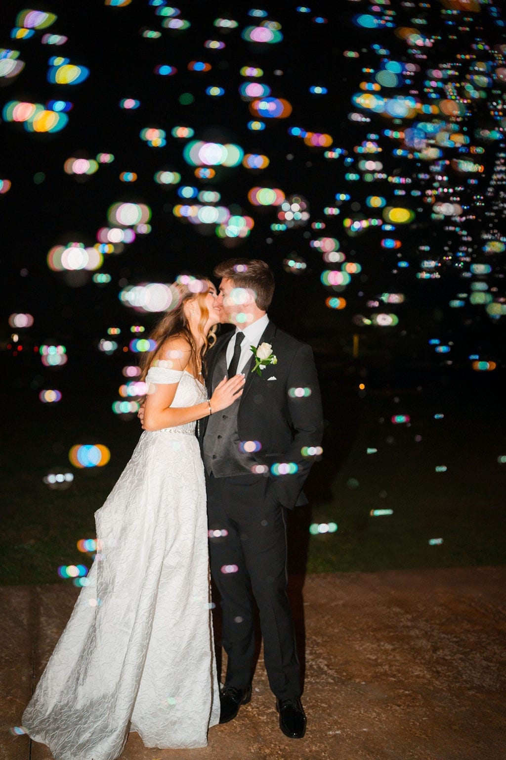 Bride and groom kissing in bubbles night wedding exit