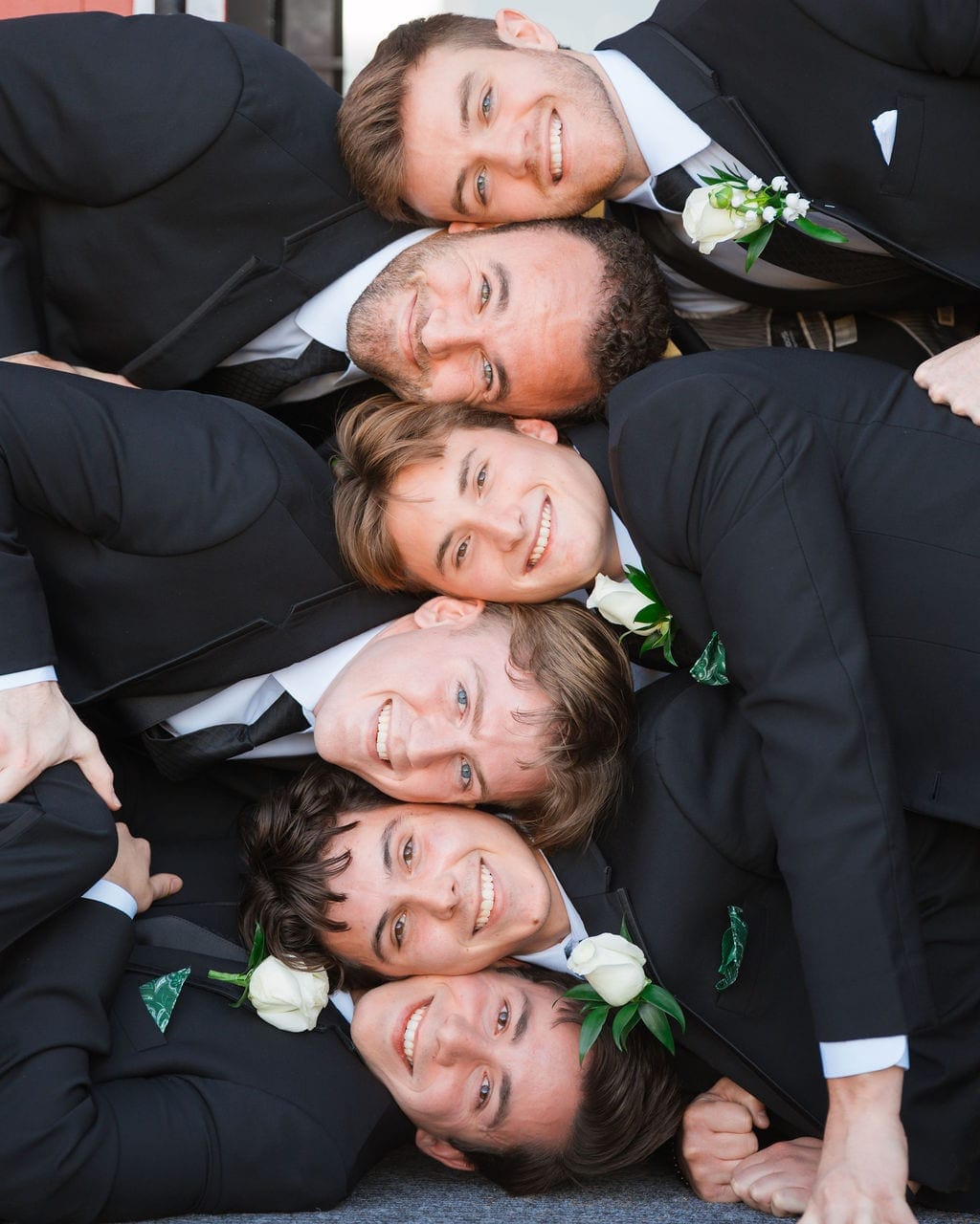 Groomsmen heads stacked in row smiling black tuxedos
