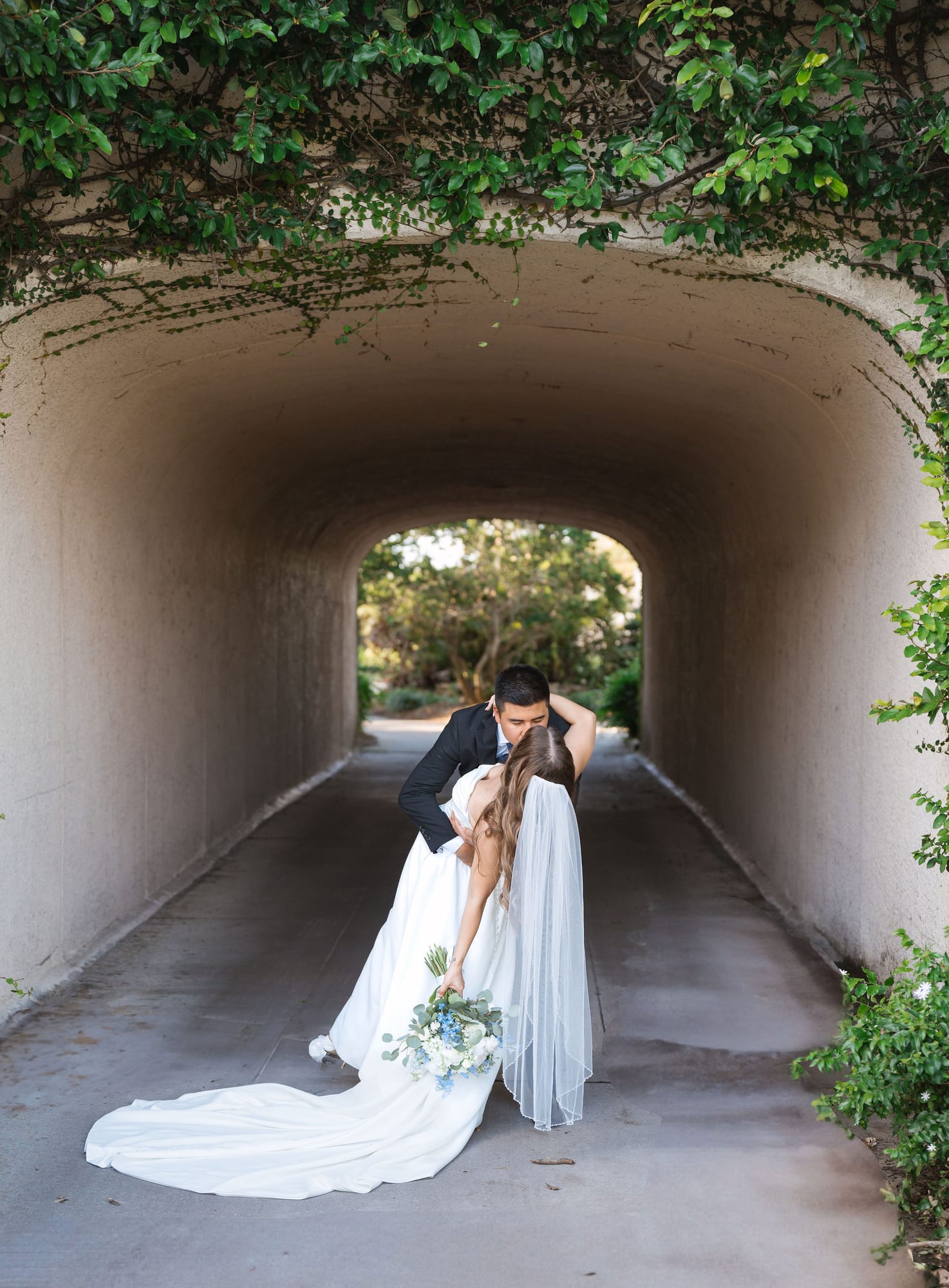 Groom dipping his bride inside the ivy covered archway