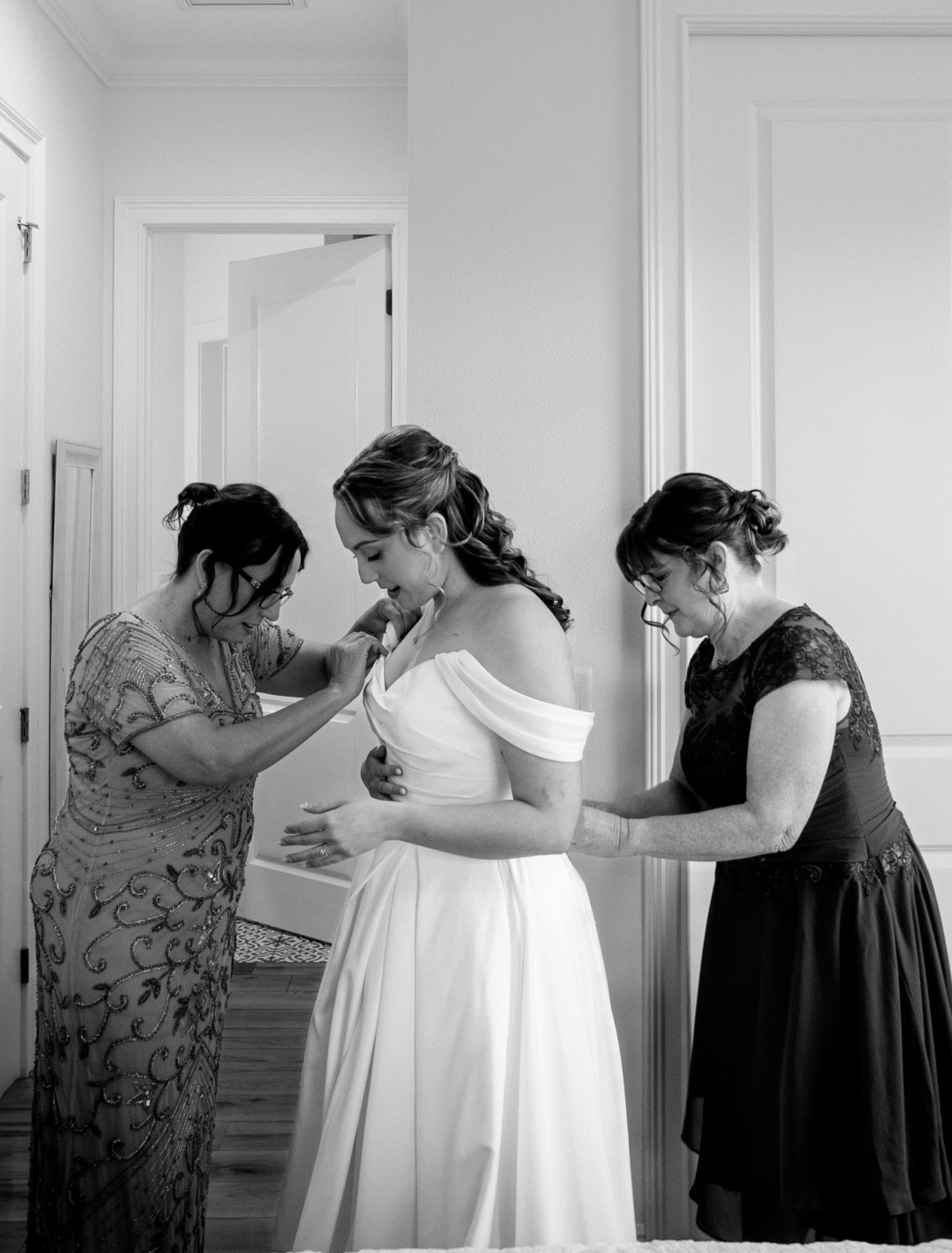 Bride being helped into her wedding dress by family in black and white