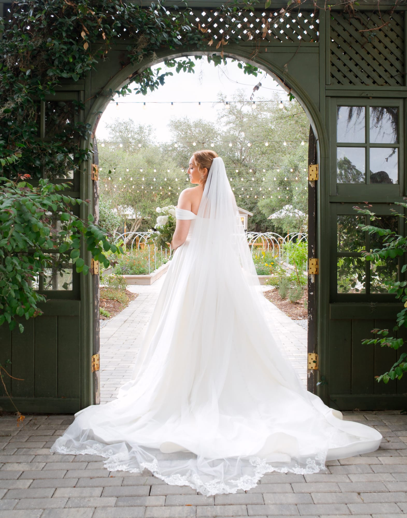 Bride standing in the glass greenhouse doorway with her cathedral veil and train spread out at Mill Pond Estate
