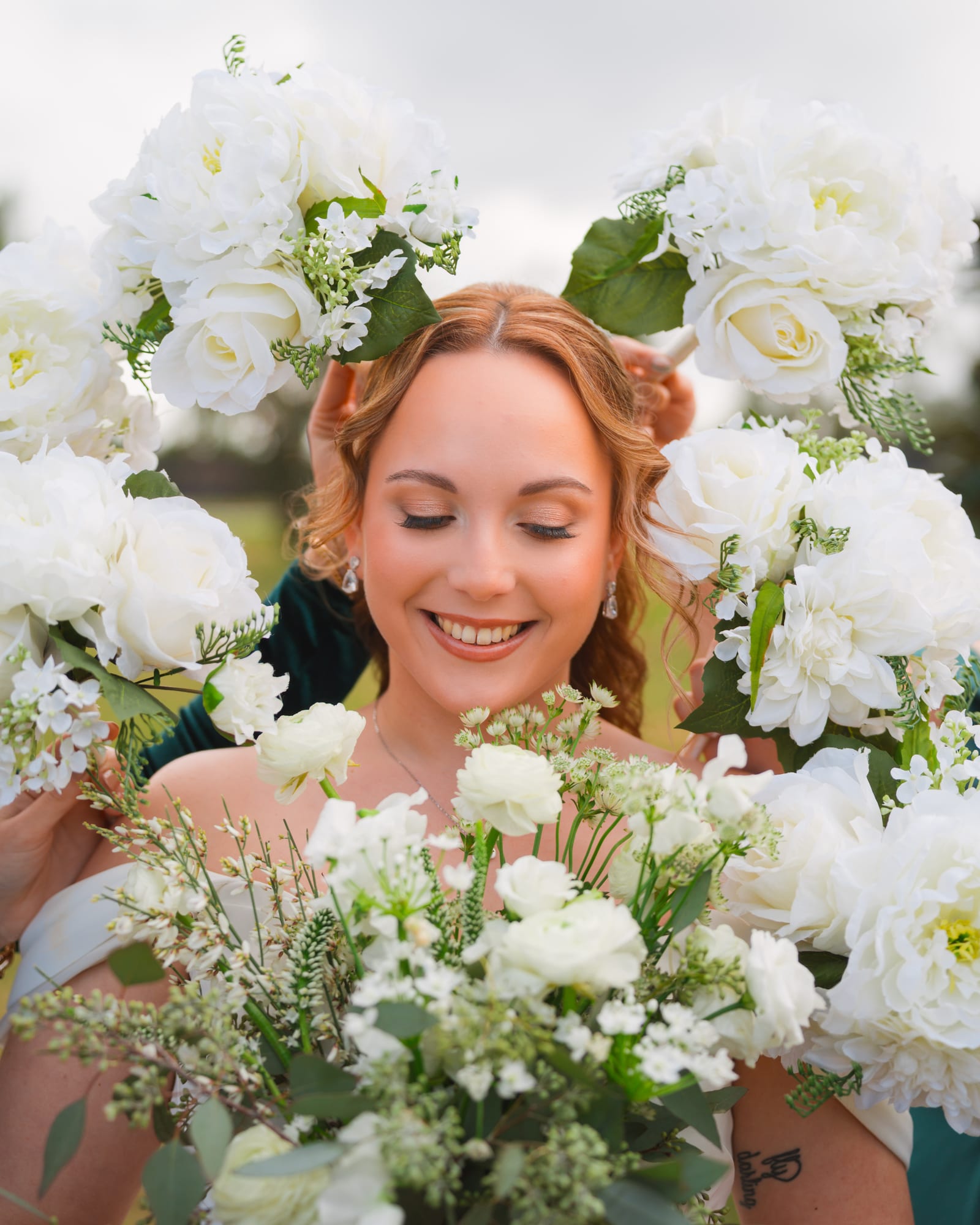 Bride smiling framed by white roses and greenery from her bouquet