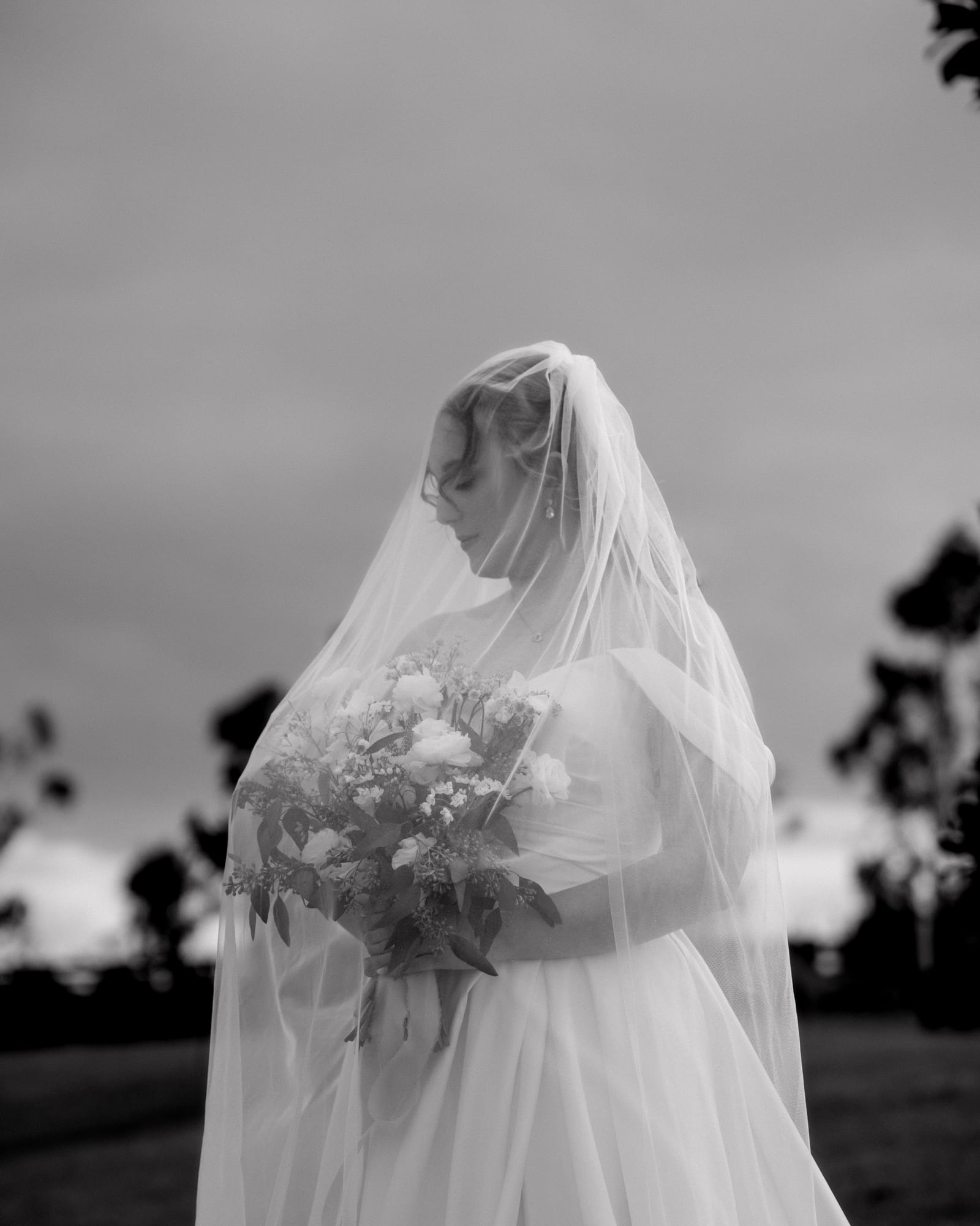 Black and white portrait of the bride beneath her veil holding her bouquet