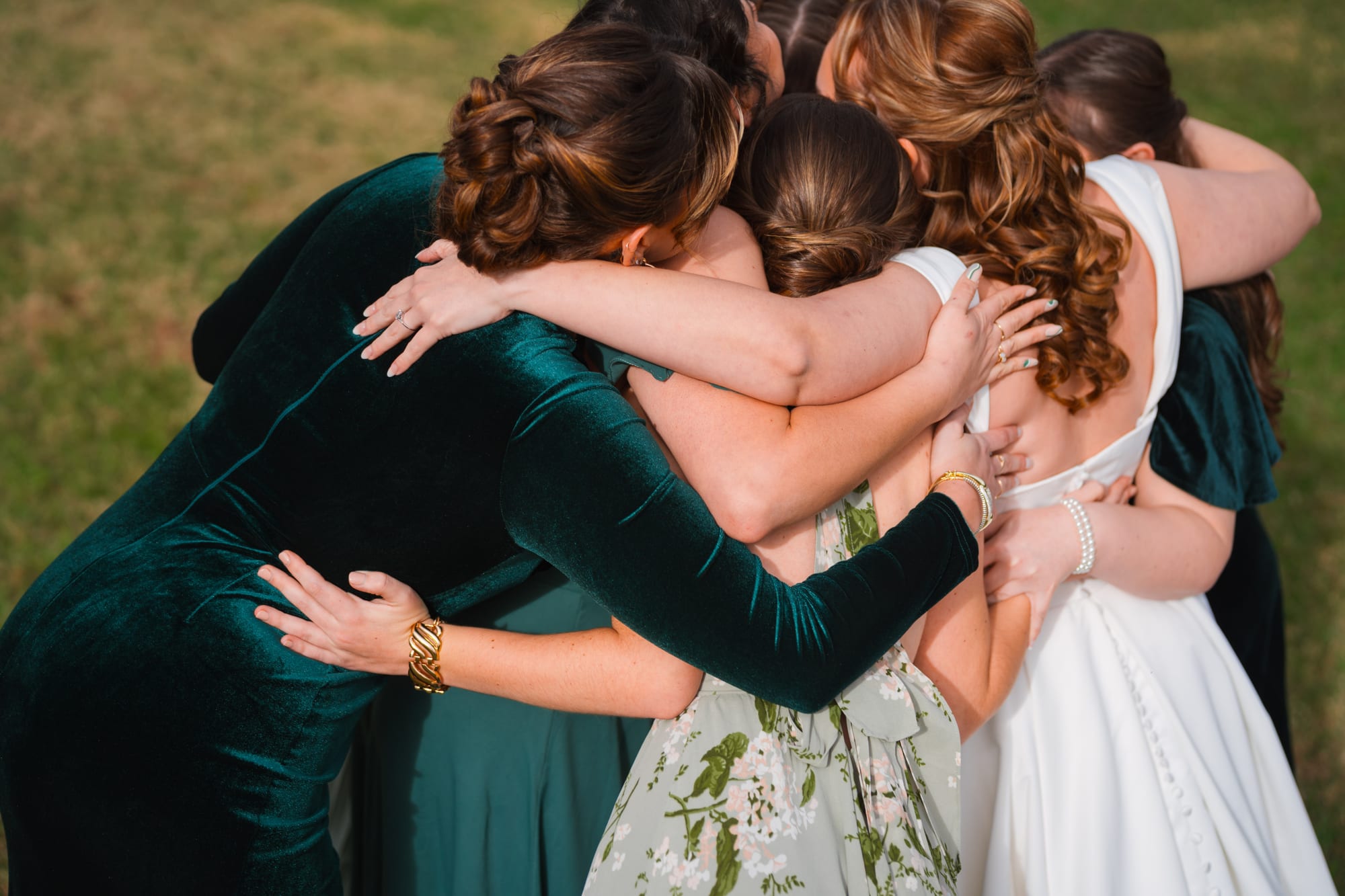 Bridesmaids in emerald green velvet dresses hugging the bride before the ceremony