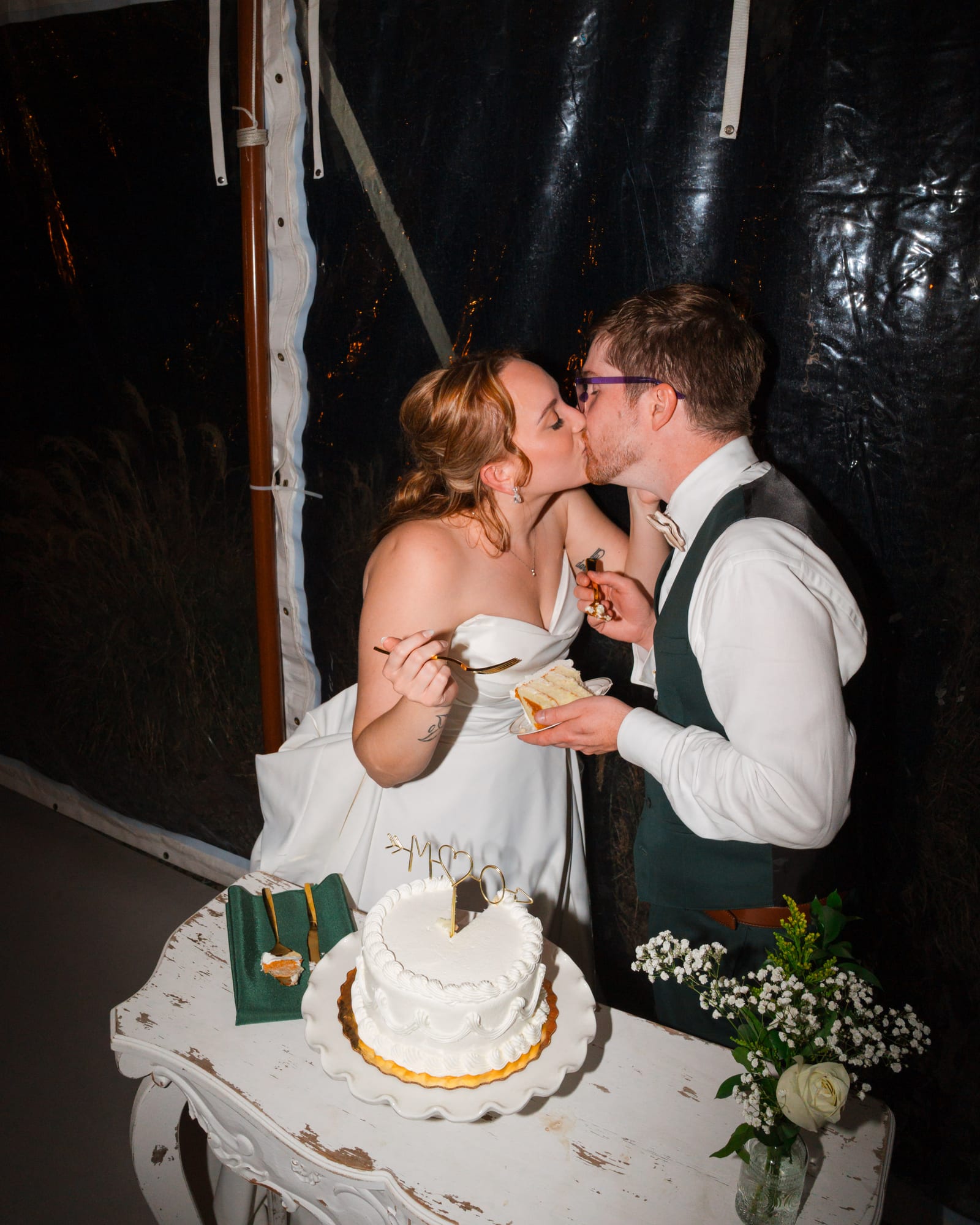 Bride and groom kissing after cutting their wedding cake in the tent