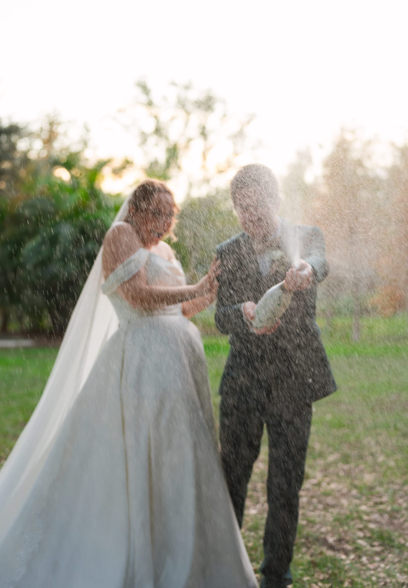 Newlyweds celebrating with a champagne spray in the field