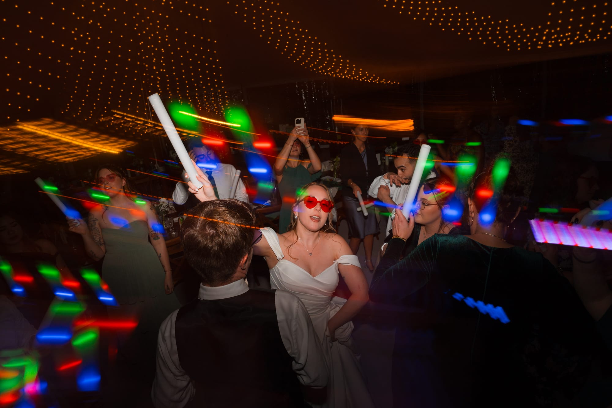 Packed dance floor lit by colorful LED batons at the reception