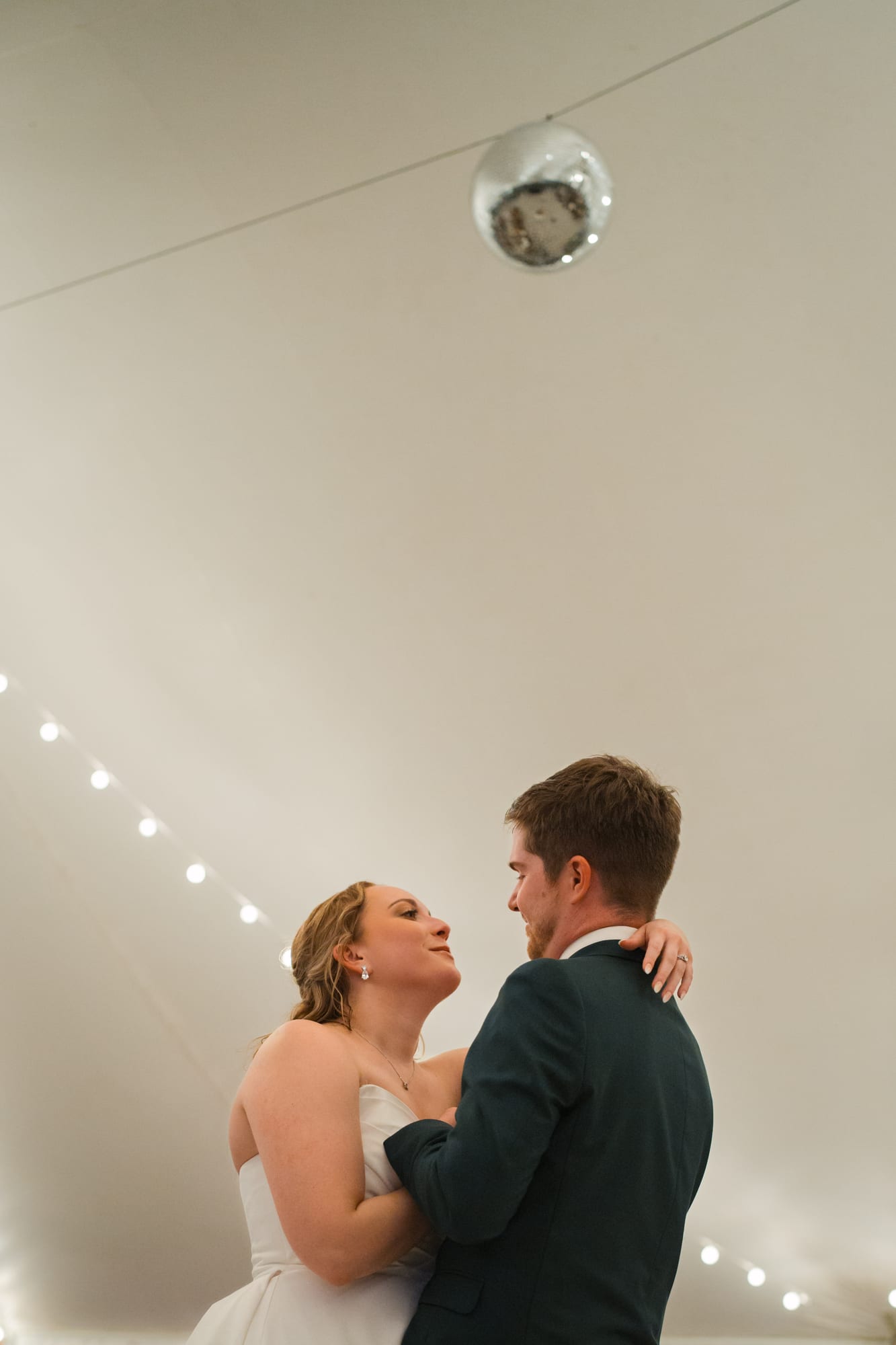 Bride and groom sharing their first dance under a disco ball in the sailcloth tent