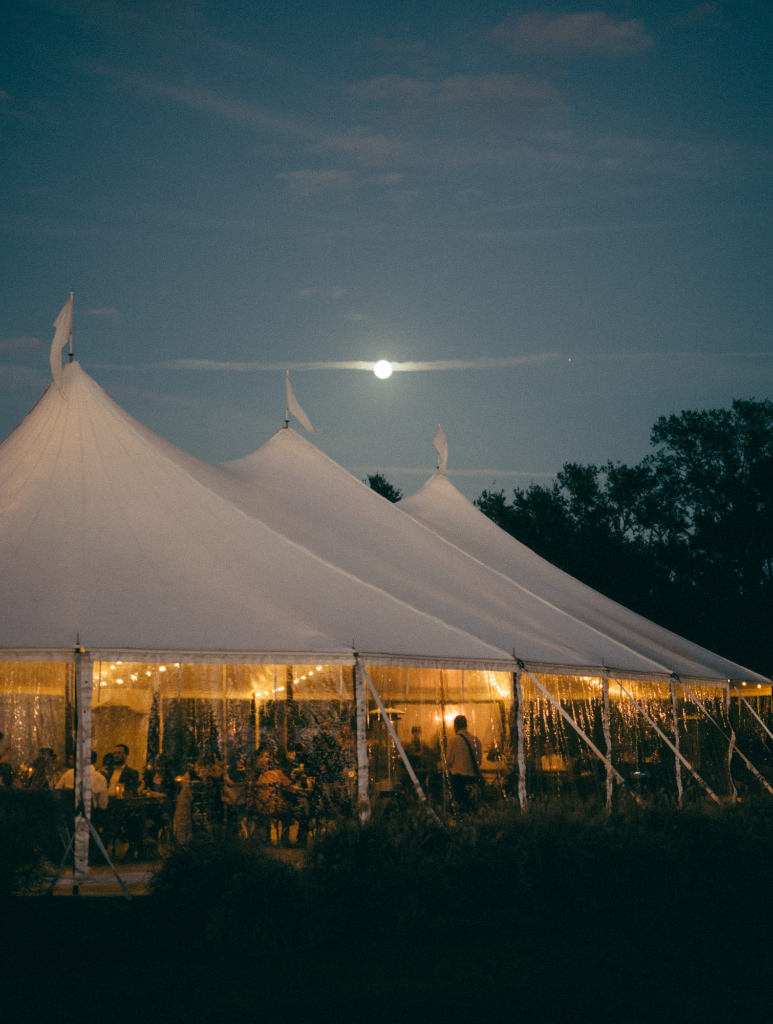 Sailcloth tents lit up under the moon at the end of the night at Mill Pond Estate