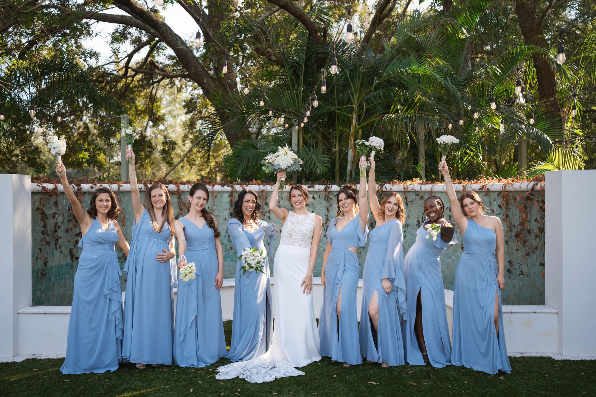 Bride with her bridesmaids in dusty blue gowns holding white bouquets