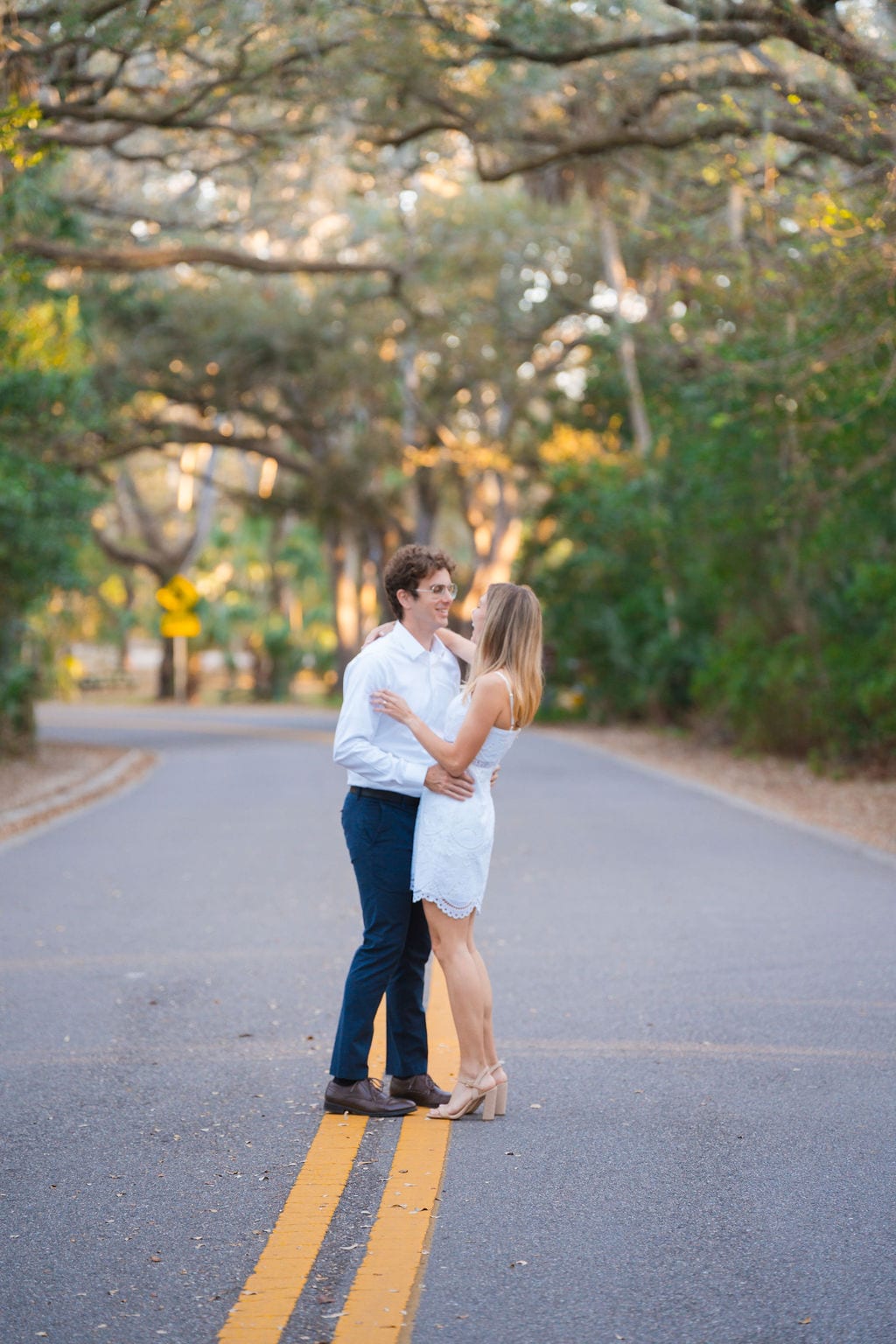 Engaged couple embracing under a live oak canopy on a road at sunset near Orlando
