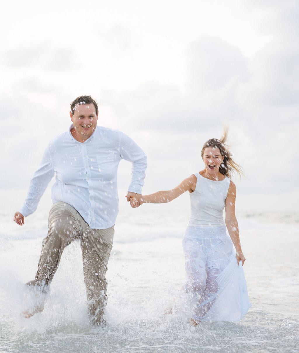 Couple running and splashing through waves during an engagement session on a Gulf beach