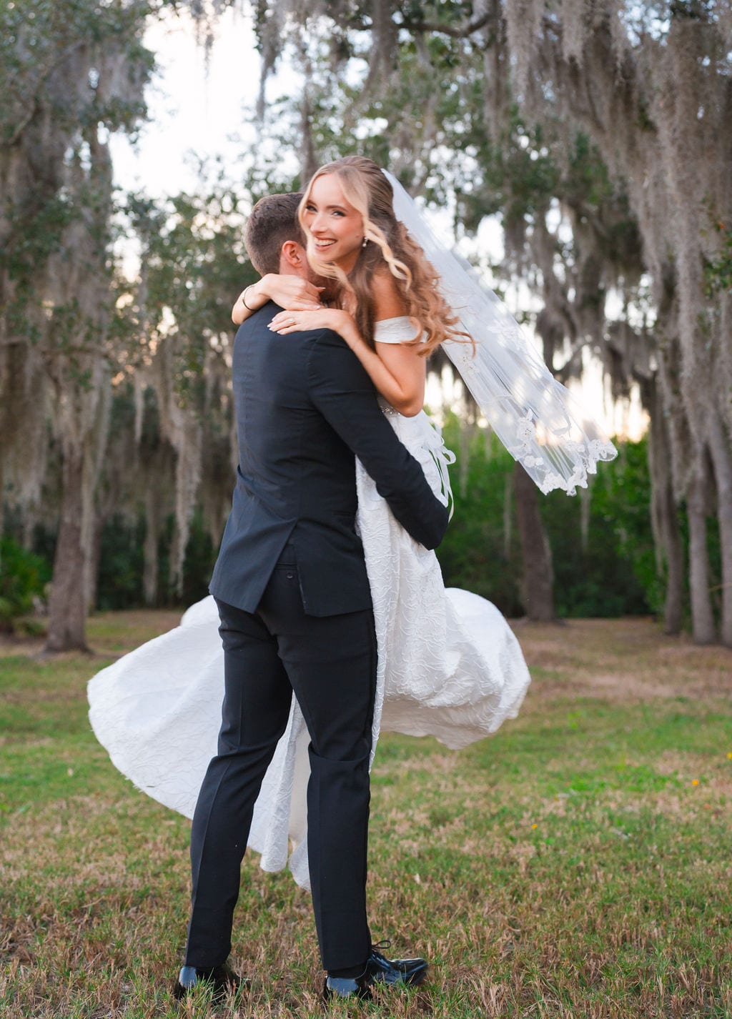 Groom lifting bride under Spanish moss oaks at sunset in Florida