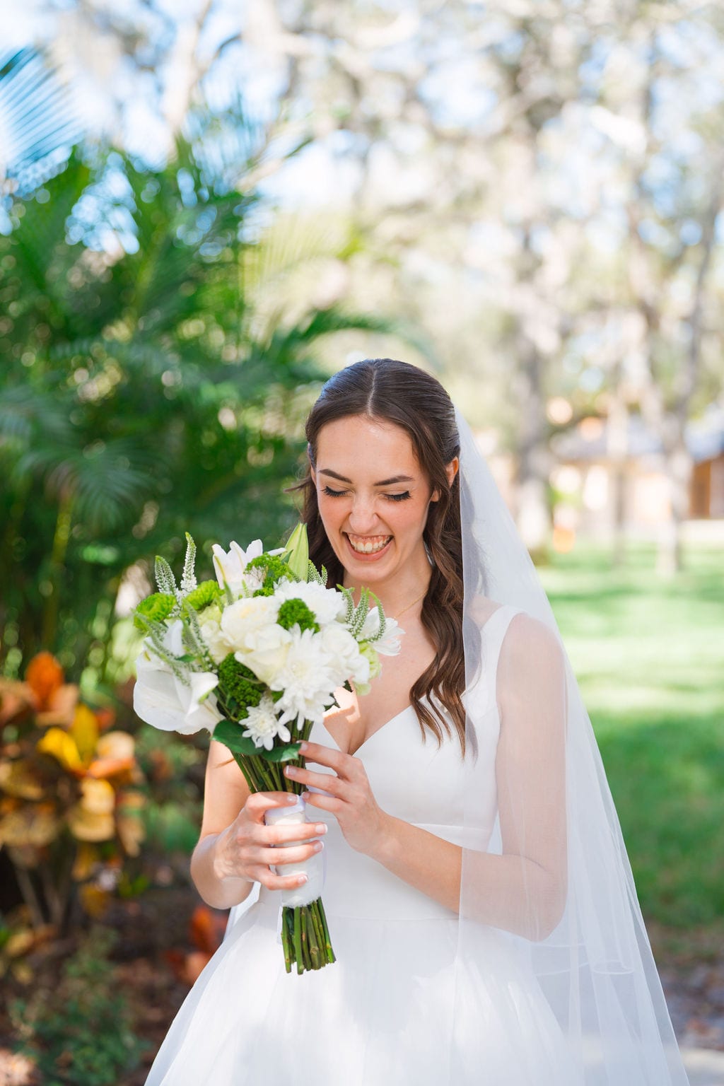 Bride laughing while holding a white and green bouquet under live oaks in Florida