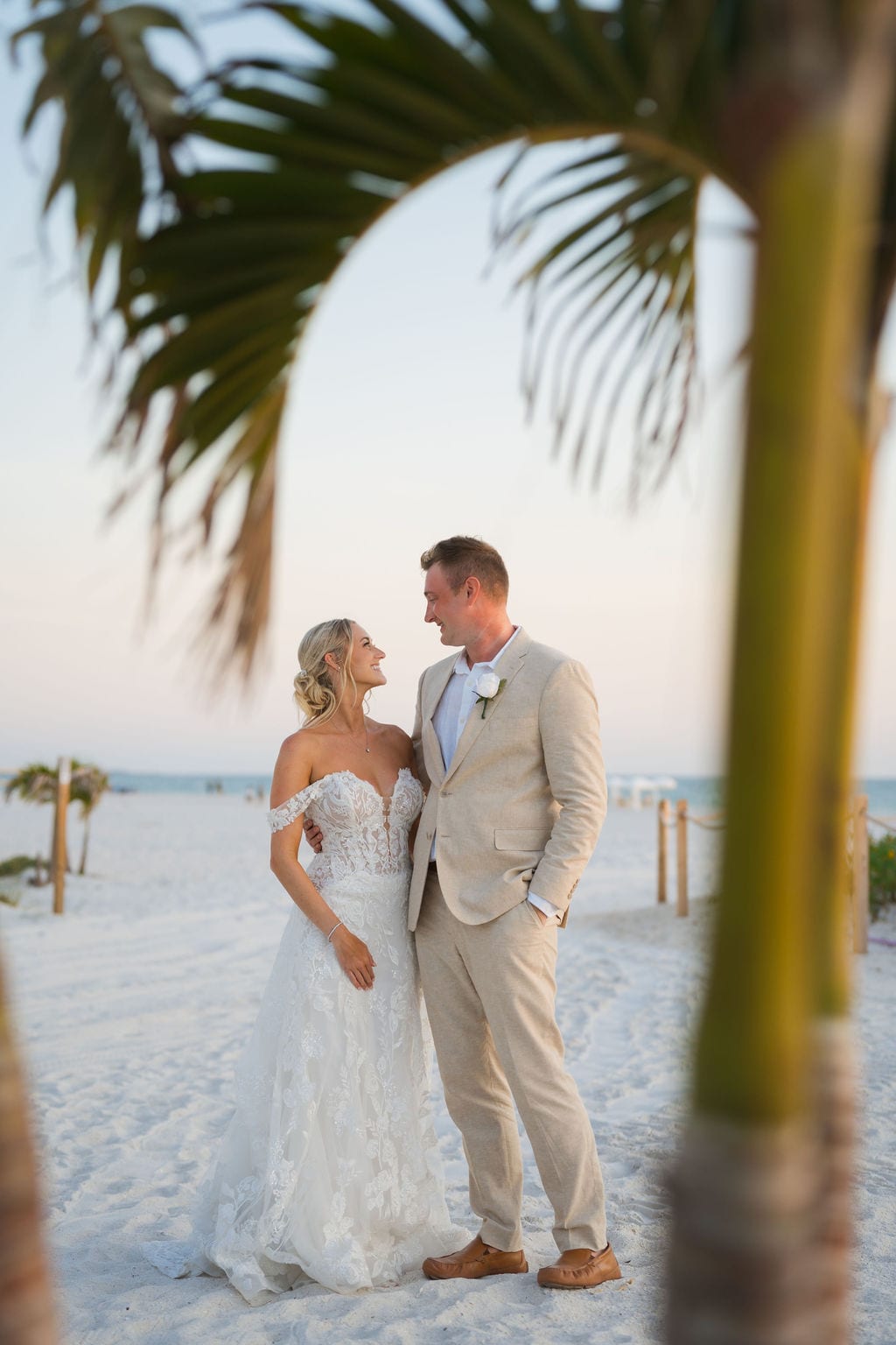 Bride and groom under a palm frond during a beach sunset portrait in Florida